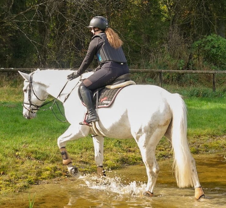 Schülerin reitet auf Pferd durch Wasser