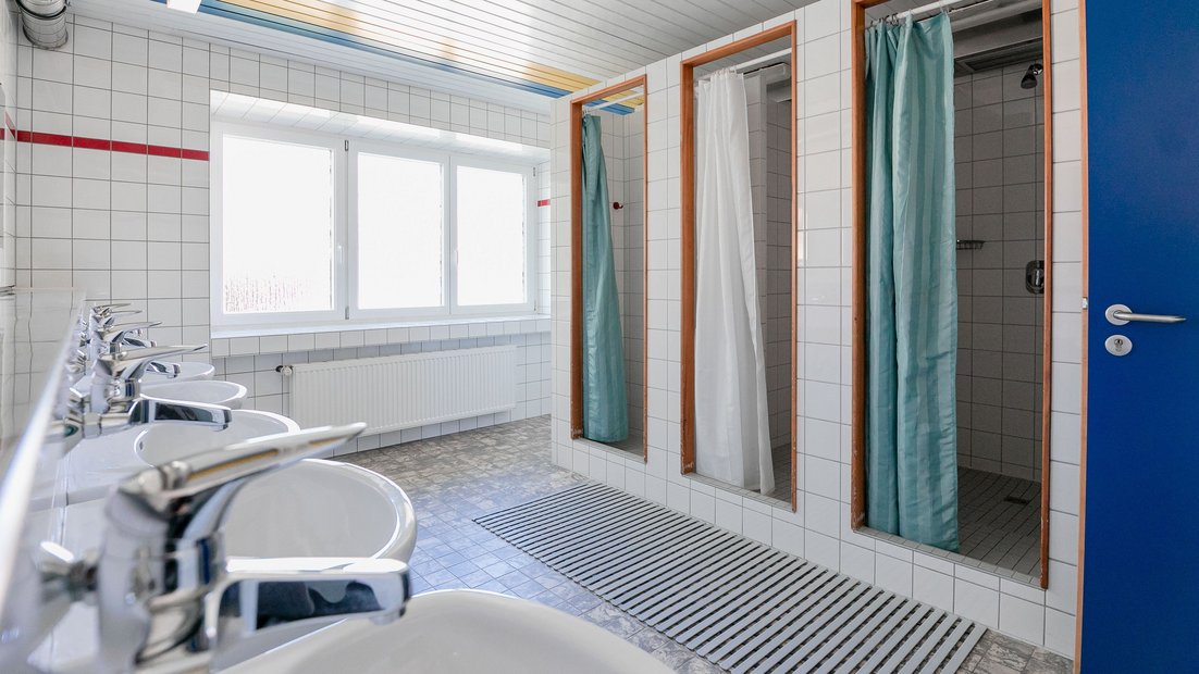 Weiß gefliestes Bad im Gartenhaus mit mehreren Waschbecken und Duschen