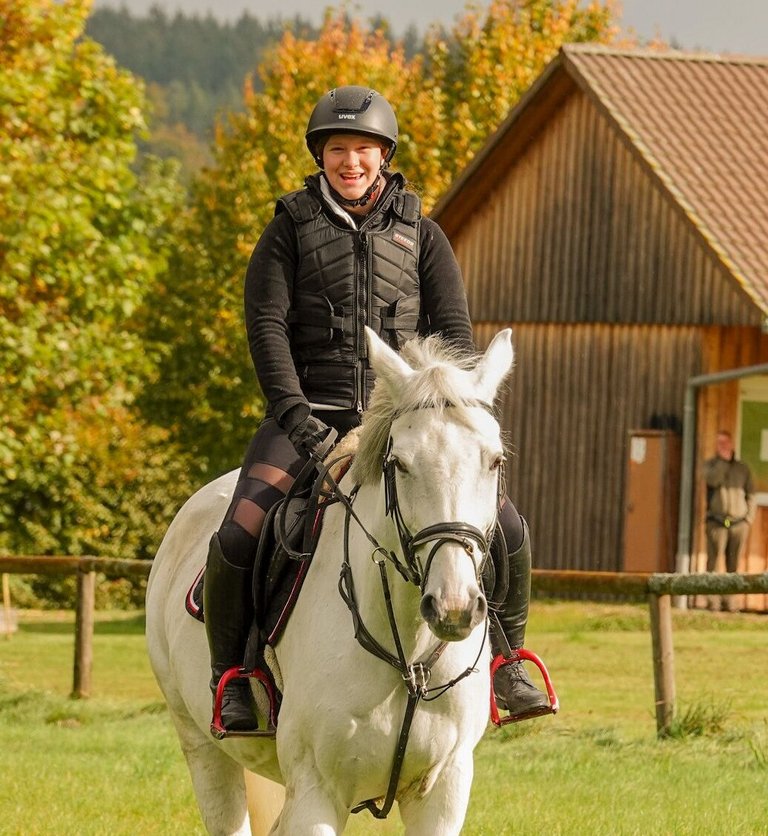 Reitsportinternat: Schülerin reitet auf Pferd über Wiese 