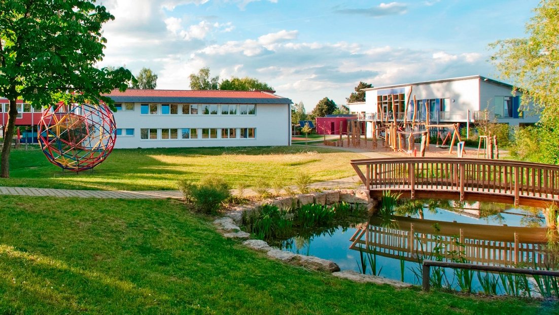 Schulgelände mit Teich und Holzbrücke