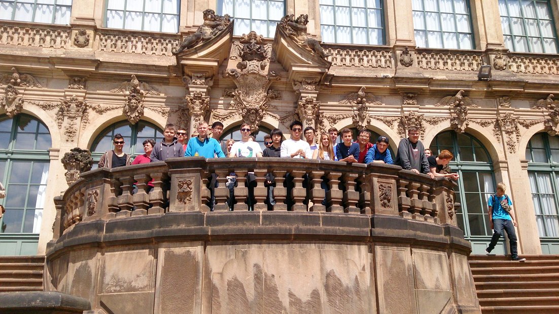 A group of schoolchildren stands on a balcony of a historic building.