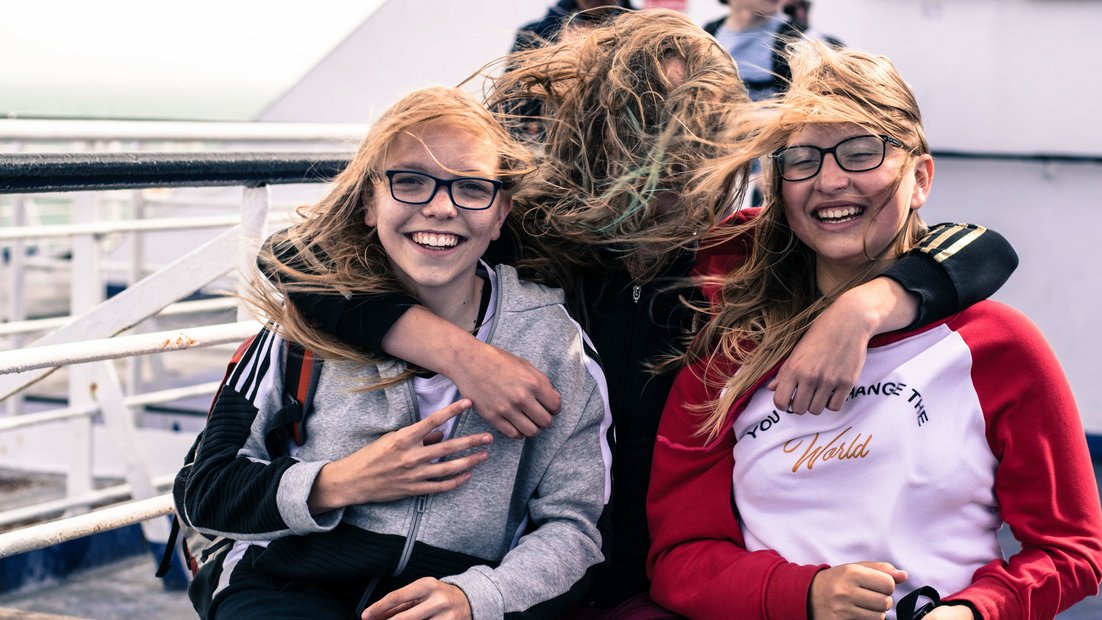 Drei Mädchen am Deck eines Schiffes lachen in die Kamera.